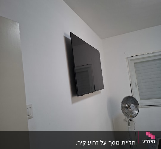 טלוויזיה מותקנת על קיר עם מאוורר עומד ליד